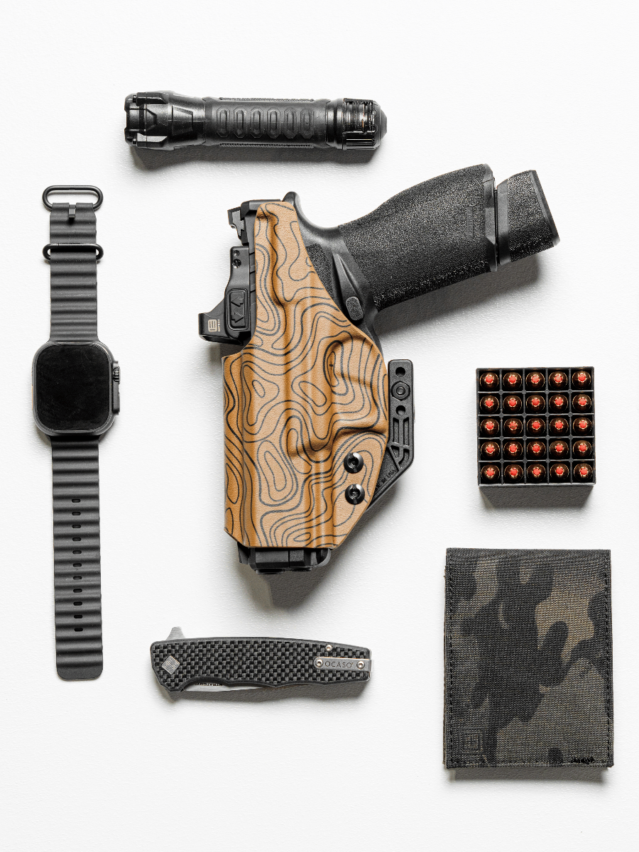 A top-down flat lay of a black handgun in a wood-grain patterned holster, surrounded by a black tactical flashlight, a black smartwatch with a dark band, a folding knife, a box of bullets, and a camouflage wallet on a white background.